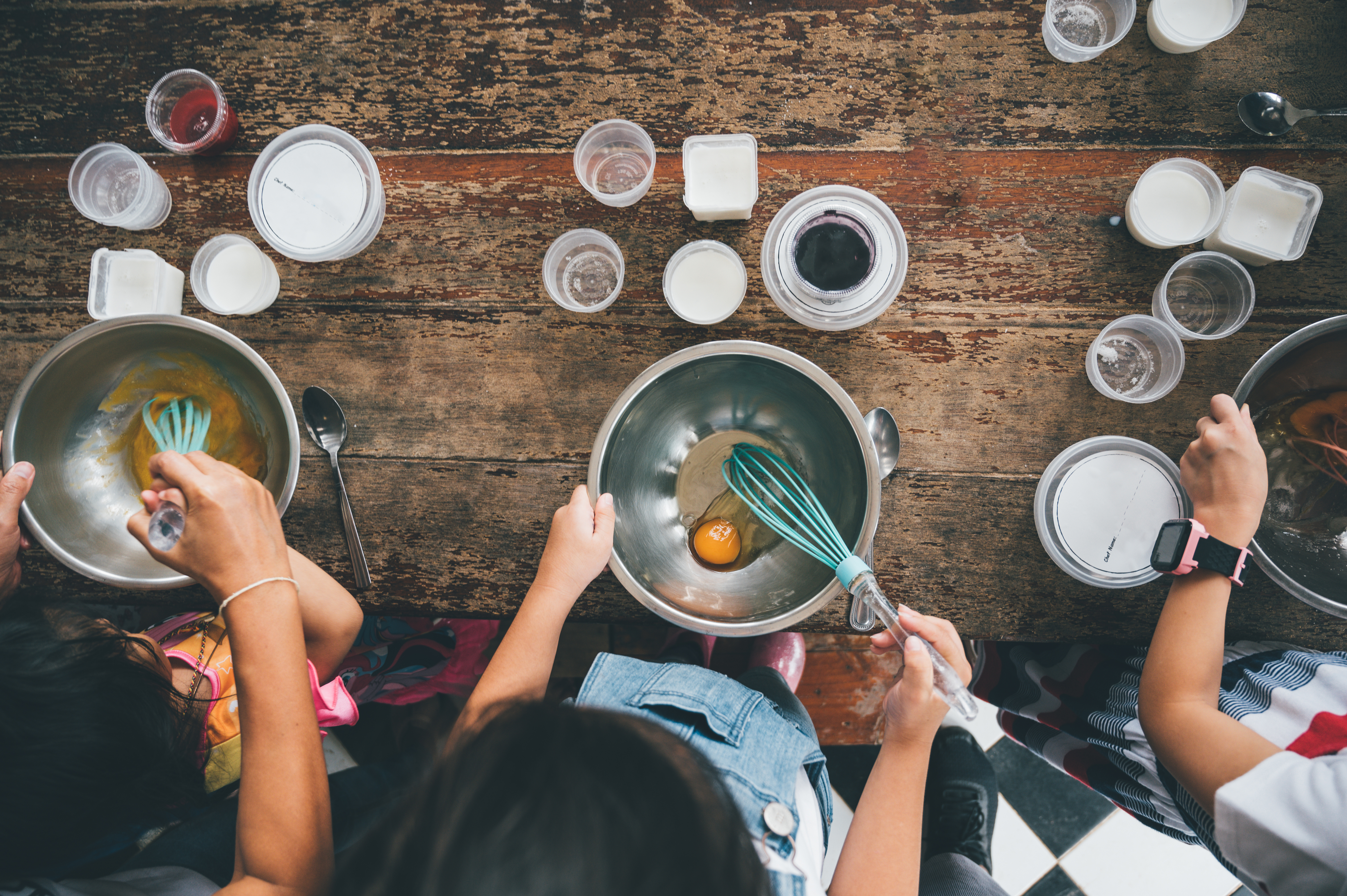 Three kids beating eggs at a wooden table